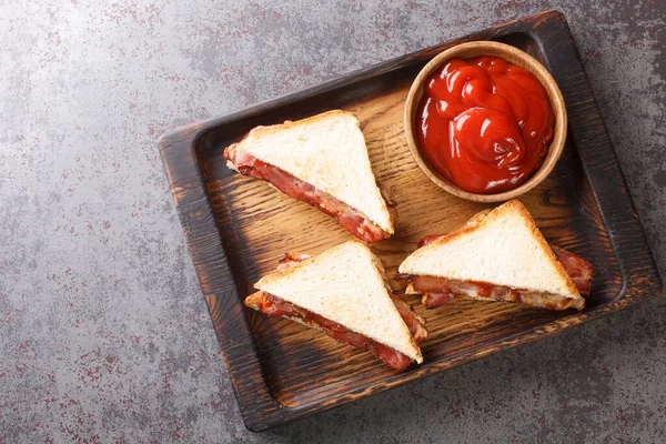 三明治与脆咸肉融化黄油和番茄酱特写在桌上的木制托盘上 从Abov的水平顶部视图 — 图库照片