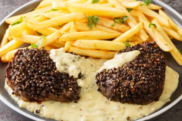 Classic French dish steak au poivre is a filet mignon with a crunchy peppercorn crust and rich Cognac sauce served with french fries close-up in a plate on the table. Horizonta