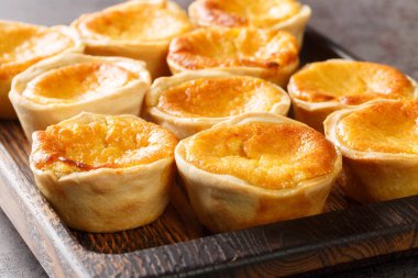 Queijadas de Sintra, masadaki ahşap tepside yakın plan tarçınlı tatlı peynir tartlarıdır. Yatay