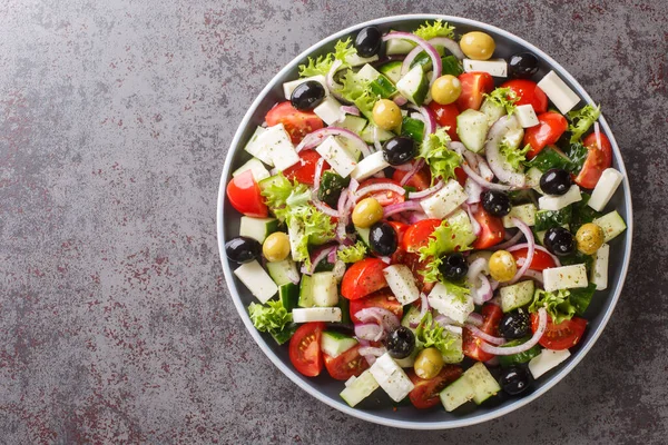 Classic Greek salad from tomatoes, cucumbers, onion with olives, oregano and feta cheese close-up in a plate on the table. Horizontal top view from abov