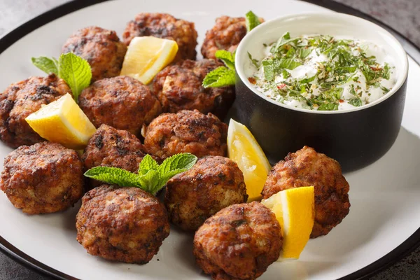 Kızarmış Keftedakia Yunan dana köftesi. Masadaki beyaz tabakta tzatziki sosu ve limonla servis ediliyor. Yatay