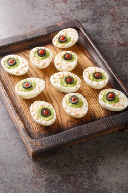 Halloween Monster eyes deviled Eggs stuffed with avocado cream wooden tray on the table. vertica