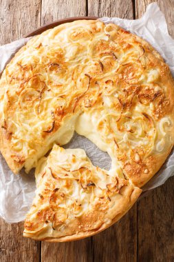 Argentinian Pizza Fugazzeta stuffed with cheese, and topped with the same sweet onions closeup in the plate on the wooden table. Vertical top view from abov