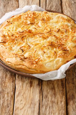 Fugazza is a common type of Argentinian pizza originating in Buenos Aires that consists of a thick pizza crust topped with onions, cheese closeup in the plate on the wooden table. Vertica