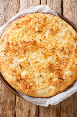 Fugazza is a common type of Argentinian pizza originating in Buenos Aires that consists of a thick pizza crust topped with onions, cheese closeup on the wooden table. Vertical top view from abov