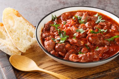 Moelas Guisadas slowly stewed chicken gizzards in tomato sauce close-up in a bowl on a wooden tray on the table. horizonta
