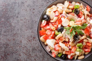 Mediterranean homemade cod salad with white beans, eggs and vegetables close-up in a bowl on the table. horizontal top view from abov
