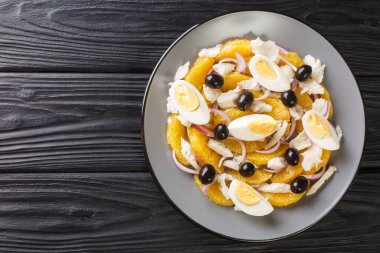 Remojon is a traditional Spanish salad made with a combination of oranges, salt cod, eggs, olive oil, olives, and wine vinegar close-up in a plate on the table. Horizontal top view from abov