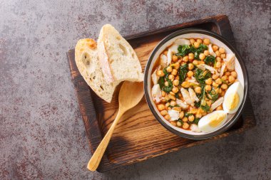 Spanish food for Easter Potaje de vigilia Chickpea stew with spinach and cod close-up in a bowl on the wooden tray on the table. Horizontal top view from abov