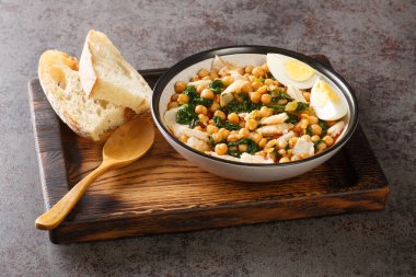 Spanish food for Easter Potaje de vigilia Chickpea stew with spinach and cod close-up in a bowl on the wooden tray on the table. Horizonta
