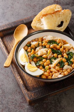 Potaje de Vigilia Spanish chickpea stew with cod and spinach close-up in a bowl on the wooden tray on the table. Vertica