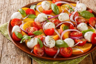 Summer peach Caprese salad with mozzarella and cherry tomatoes close-up in a plate on a wooden table. Horizonta