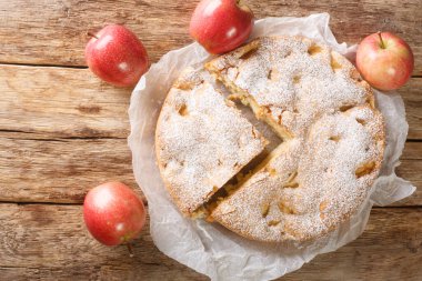 Sliced Apple pie sharlotka and red apples on a wooden table. Horizontal top view from abov