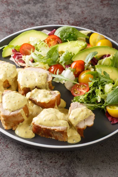 Baked pork tenderloin with mustard cream sauce and fresh vegetable salad close-up in a plate on the table. Vertica