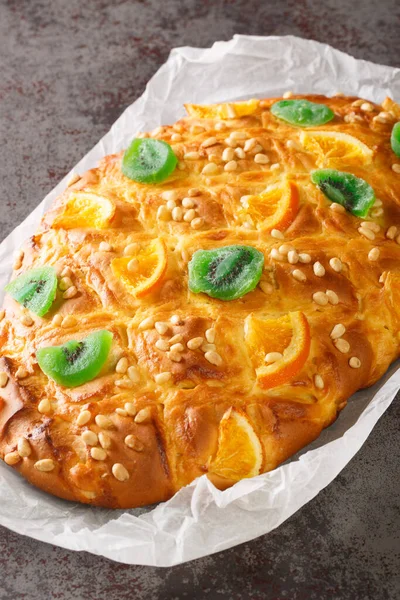Coca de Sant Joan is one of the most popular coques, yeast breads, in Catalonia with cream and decorated with pine nuts, candied fruit closeup on the paper on the table. Vertica