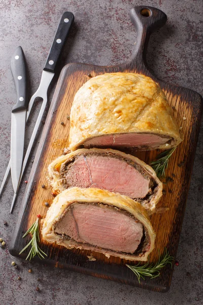High angle beef wellington cooking or boeuf en crout cut into slices on a chopping board grey background. Vertical top view from abov