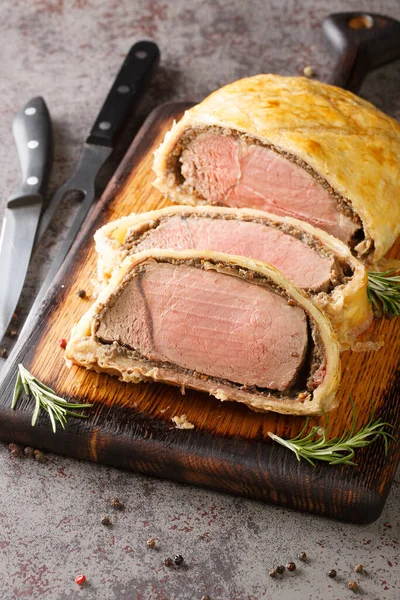 High angle beef wellington cooking or boeuf en crout cut into slices on a chopping board grey background. Vertica