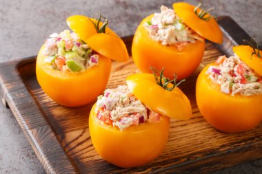 Tasty appetizer yellow tomatoes stuffed with tuna salad and vegetables close-up on a wooden tray on the table. Horizonta