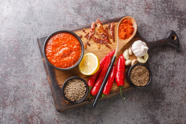 Hot chilli pepper sauce paste harissa, Arabic cuisine adjika on the bowl on wooden board with ingredients closeup. Horizontal top view from abov