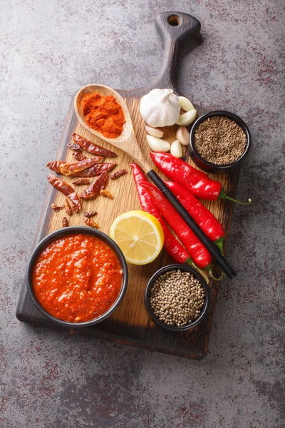 Hot chili pepper sauce paste Harrisa in arabic, tunisian cuisine Adjika in Caucasian kitchen on the bowl on wooden board closeup. Vertical top view from abov