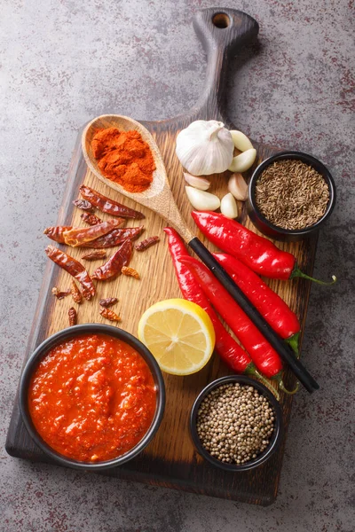 Traditional sauce with hot chili pepper paste harissa in bowl on wooden board with ingredients closeup. Vertical top view from abov