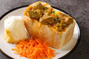 South African cuisine Bunny chow mutton curry in a hollowed out half a loaf of bread closeup on plate on the table. Horizonta