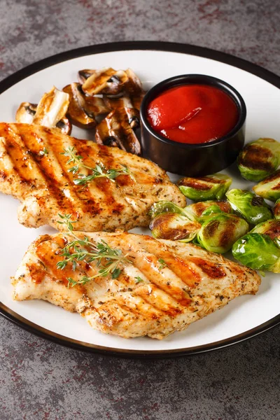 Grilled chicken fillet with Brussels sprouts, mushrooms and spicy tomato sauce close-up in a plate on the table. vertica