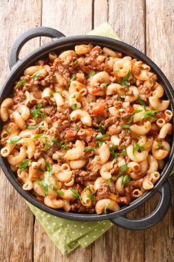 Soğan, domates sosu ve ahşap masadaki tavada yakın plan makarna ile pişirilmiş hafif yiyecek kıyması. Yukarıdan dikey üst görünüm