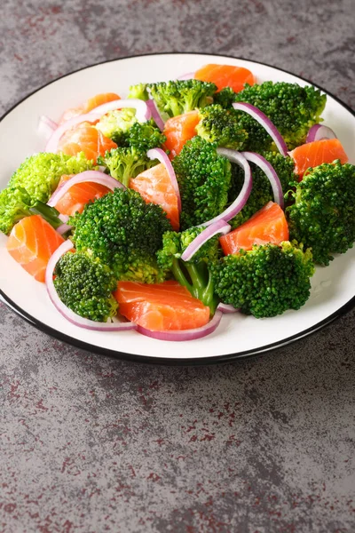Dietary salad of steamed broccoli, salted salmon and red onion close-up in a plate on the table. Vertica