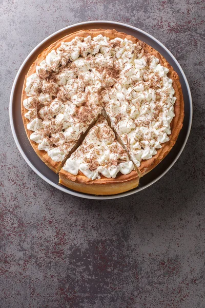 Sweet pie with a filling based on rice pudding topped with whipped cream and chocolate chips close-up in a plate on the table. Vertical top view from abov