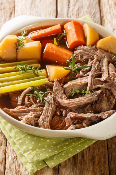 Homemade Slow Cooker Pot Roast with Carrots, Celery and Potatoes closeup in the bowl on the wooden table. Vertica