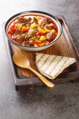 Havuçlu, patatesli, yeşil bezelyeli ve domatesli mis kokulu kuzu güveci ahşap bir tahtanın üstünde. dikey