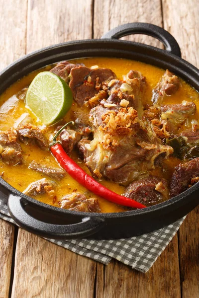 Lamb Curry or Indonesian Gulai Kambing for Eid closeup on the pan on the wooden table. Vertica