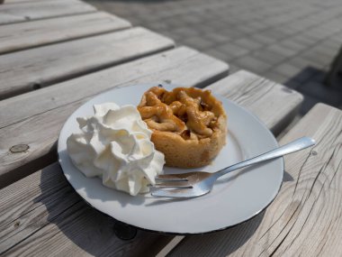 Elmalı turta, güneş ışığında çırpılmış kremayla ahşap bir masada.