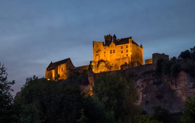 Beynac kasabası üzerinde akşam saatlerinde aydınlatılmış Chateau de Beynac kuleleri Fransa 'nın Dordogne nehrinin bir kıvrımında kayalara tutunur.