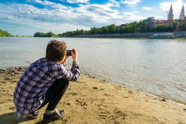 SZEGED, HUNGARY - 21 Mayıs. 2022: Genç kız Tisza nehrinin sahilinde fotoğraf çekiyor