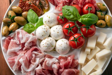 Salam, jambon, mozzarella, domates ve fesleğen gibi çeşitli İtalyan yemekleriyle dolu bir tabak.