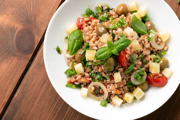 top view of pearl barley with vegetables and basil on white plate