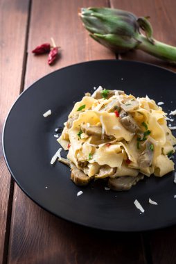 Enginarlı ahşap masa, pişmiş İtalyan makarnası. 