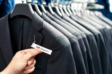 Etiketli organik takım elbiseler. Etik erkek modası. Sürdürülebilir perakende mağazasında müşteri. Doğal kumaş ve tekstil ürünü. Bir sıra şık elbise askıda..