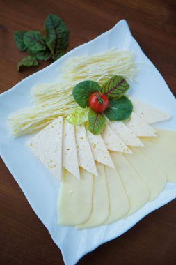 Yeşillikle süslenmiş beyaz bir tabakta dilimlenmiş peynir..