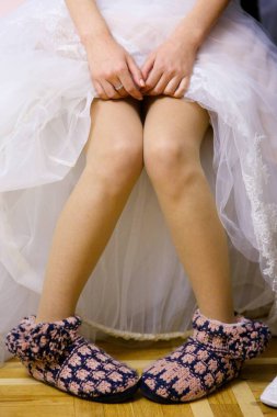 Gelinin bacakları gelinliğin altında ayakkabısız oturuyor. Ayak tığ işi çorap terlikleri..