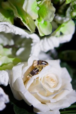 Metalden yapılmış alyanslar bir buket taze çiçeğin üzerinde duruyor. Tatil ve tören kavramı.