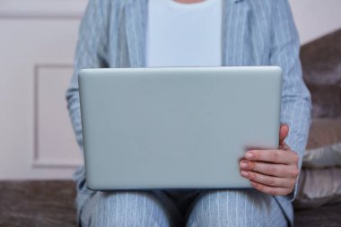 Dizüstü bilgisayar, koltukta oturan ofis elbiseli bir kızın kucağında yatıyor. Yakın plan. Odanın içinde fotoğraf var..