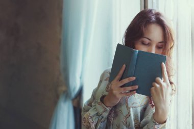 Odanın penceresinde oturmuş kitap okuyan genç ve güzel bir kız. Geliştirme ve eğitim kavramı.