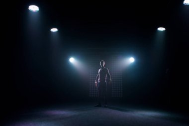 Günlük kıyafetli bir adam karanlık bir sahnede dans pozu verir. Arka ışıklandırma sahne ışığı. Bir dansçının silüeti..