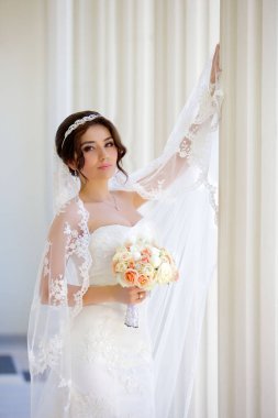 Yürüyüşteki mutlu, güzel, genç gelin. Duvağı olan beyaz elbiseli bir kız. Ceketli damat. Arka planda beyaz sütunlar var..