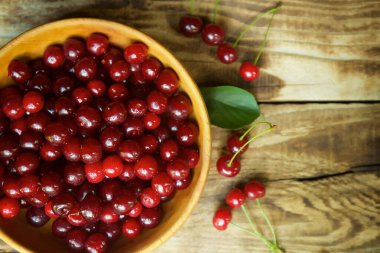 Fresh red berry cherry lies in a wooden bowl on the wooden surface of the table.