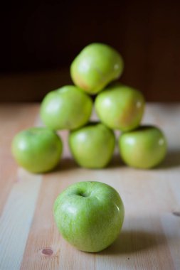 Many green large apples lie on the wooden surface of the table.