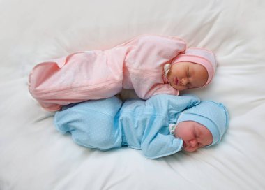 Two newborn baby twins boy and girl are in pink and blue suits on a white blanket.